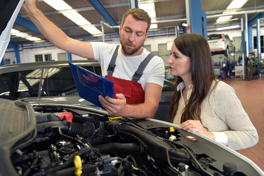 Kundendienst in der KFZ Werkstatt Automechaniker beraet Kundin wegen Reparaturauftrag arbeitsablaeufe-organisieren