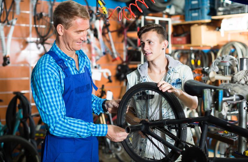 Junger Mann lässt sein Fahrrad vom Mechaniker prüfen/reparieren - Auftragsabwicklung im Handwerk