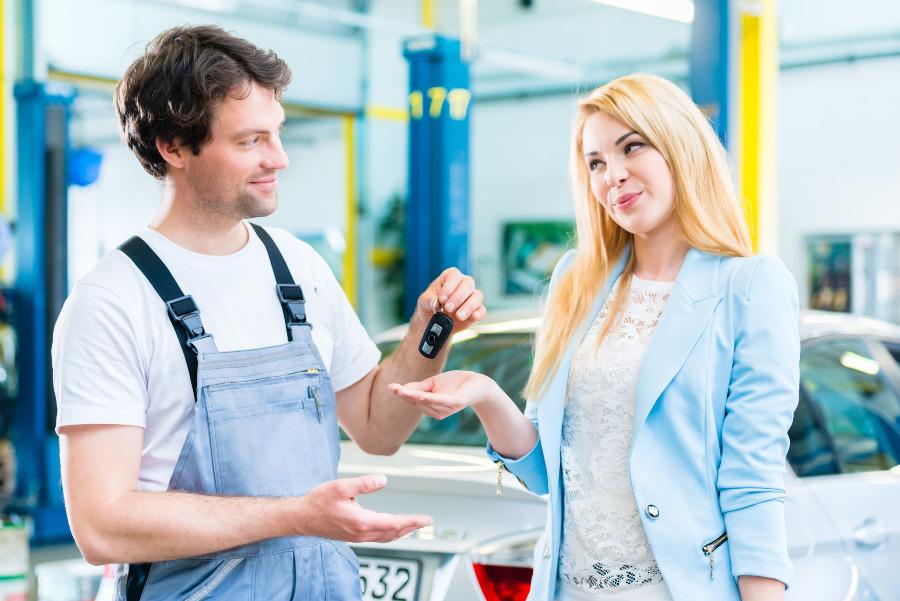 Ein Mechaniker übergibt nach erfolgreicher Reparatur den Fahrzeugschlüssel an eine zufriedene Kundin 