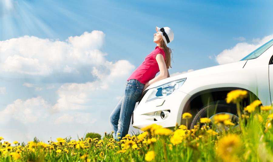Junge Frau lehnt an Auto - Symbol für Autofrühling
