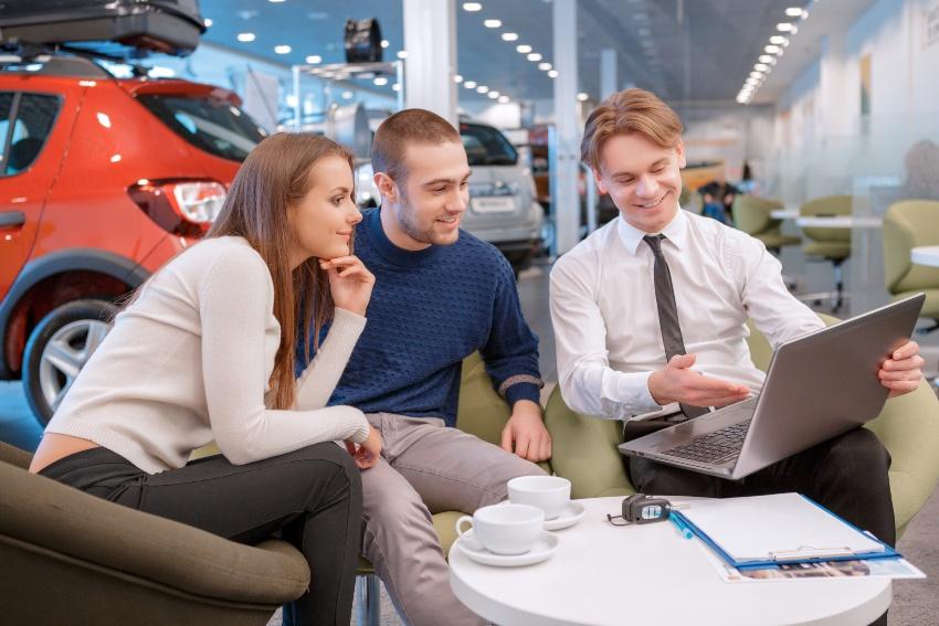 Junges Paar in einem Autohaus im Gespräch mit Autoverkäufer - Neueröffnung im Autohaus 