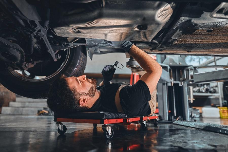KFZ-Mechaniker arbeitet unter einem Auto - Arbeitsschutz in der Kfz-Werkstatt ist essenziell