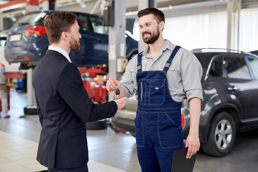 Automechaniker gibt Kunden den Autoschlüssel zurück - Werkstattservice verbessern durch Kundenorientiertheit