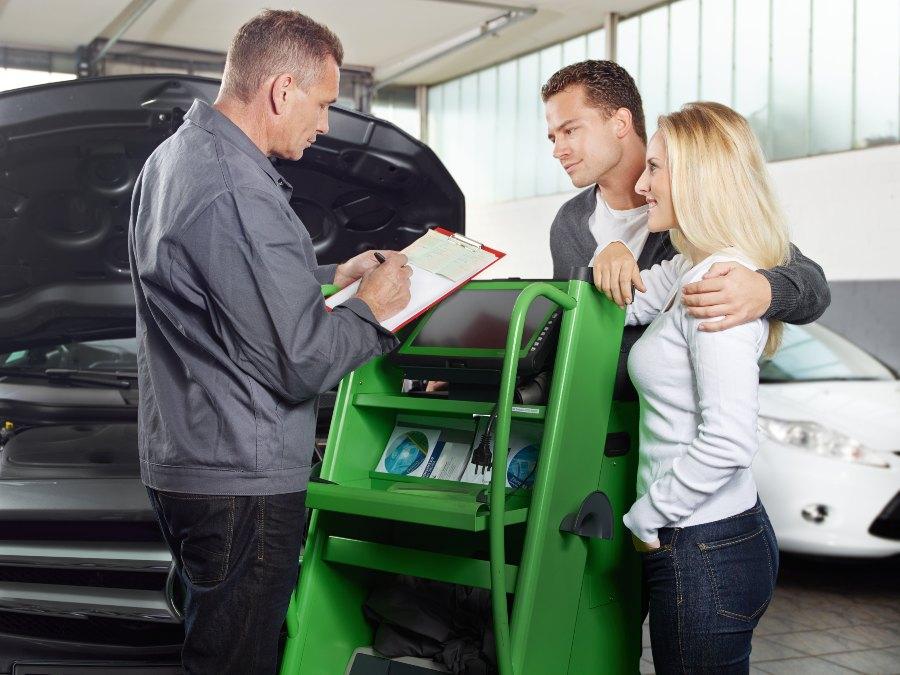 In der Werkstatt bespricht ein Mechaniker mit einem jungen Paar den Reparaturauftrag für ihr Fahrzeug