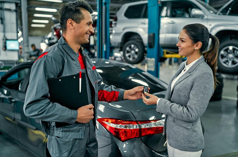 Ein Mechaniker übergibt einer Werkstattkundin einen PKW-Schlüssel 