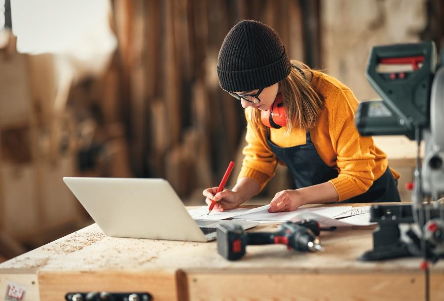 Junge Handwerkerin zeichnet, im Vordergrund ein Laptop
