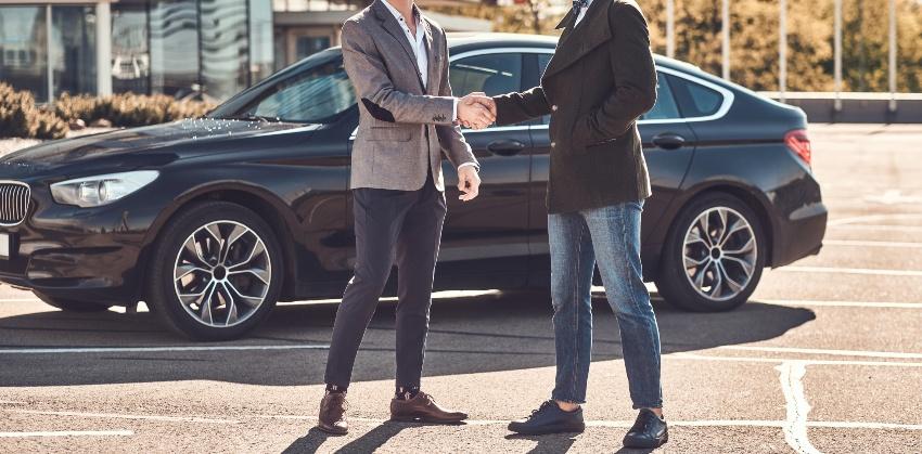Zwei Männer geben sich die Hand, im Hintergrund ein Auto
