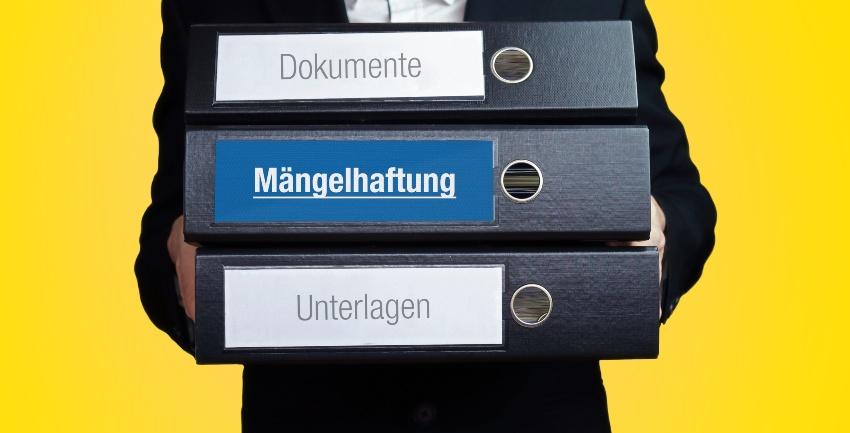 Mann trägt diverse Aktenordner, eine lautet "Mängelhaftung" - Der gewerbliche Kaufvertrag für Autos