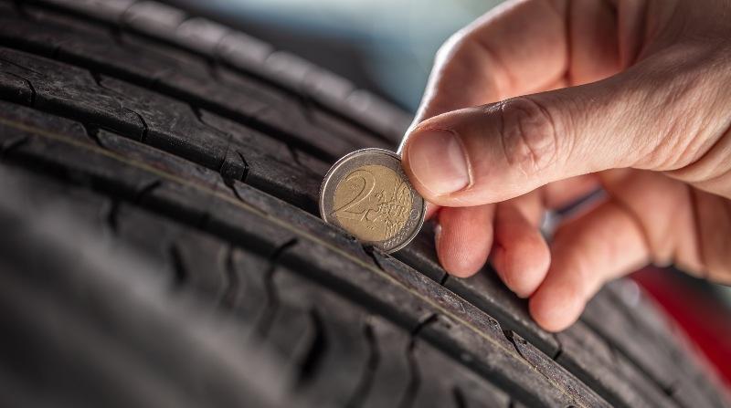 Jemand prüft die Profiltiefe eines Autoreifens mithilfe eines 2-EUR Stücks - Winterreifen wechseln