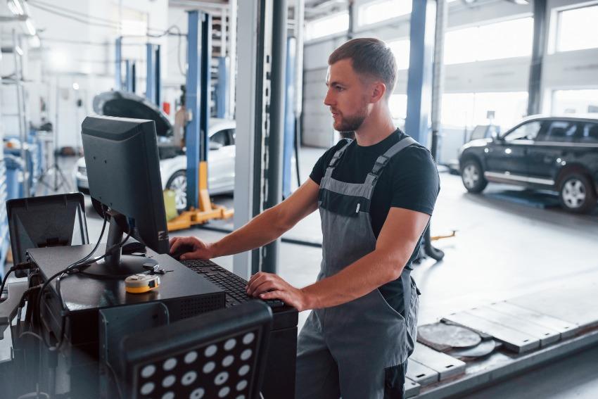 Junger Automechaniker steht am Computer - Werkstatt aufgeräumt